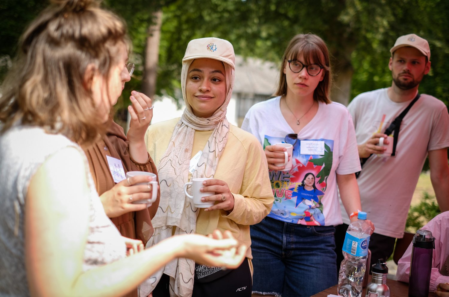 Alumni stehen im Freien mit Tassen in der Hand zusammen und unterhalten sich