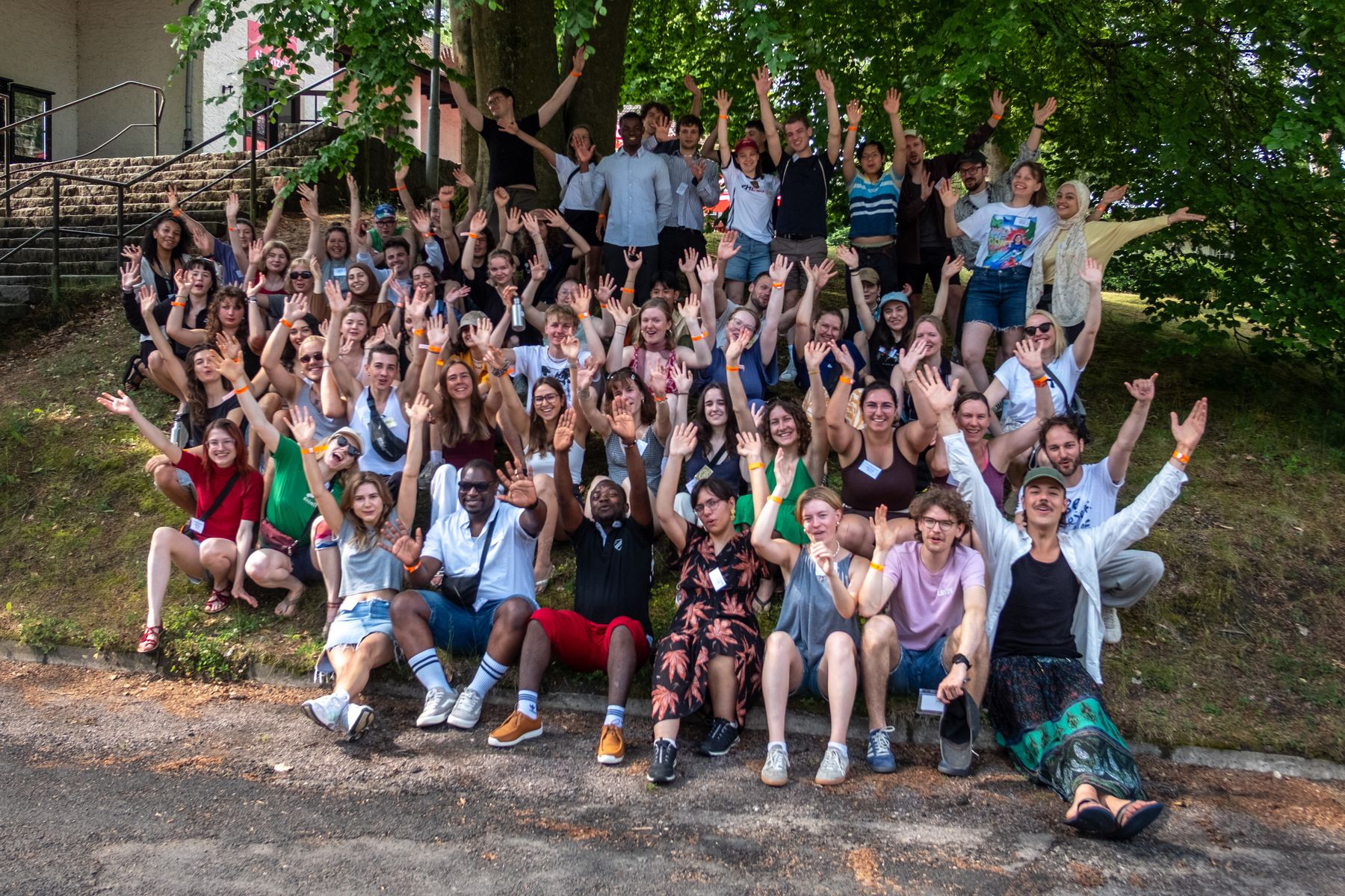 Große Gruppe von kulturweit-Alumni winkt fröhlich in die Kamera, aufgenommen bei der Zukunftskonferenz am Werbellinsee